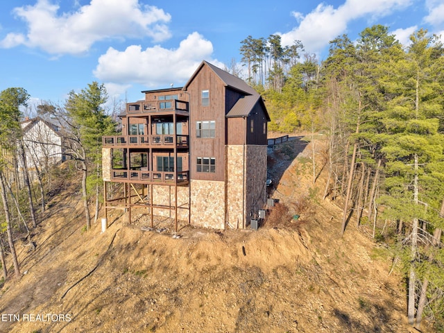 back of house featuring a balcony, stone siding, and metal roof