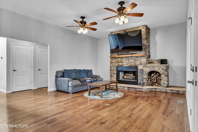 living room with hardwood / wood-style flooring, a stone fireplace, and ceiling fan