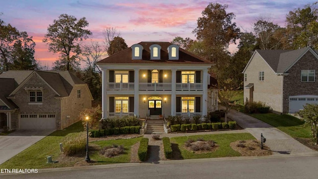 greek revival house with a balcony, an attached garage, a yard, covered porch, and concrete driveway