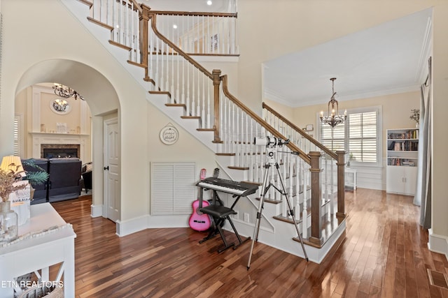 staircase featuring a high ceiling, hardwood / wood-style flooring, ornamental molding, and a notable chandelier