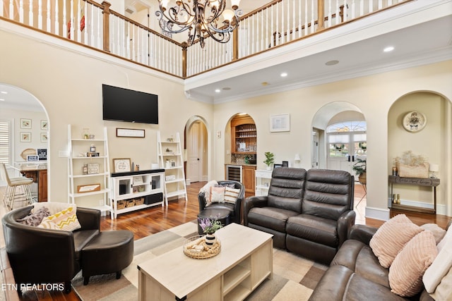 living room featuring beverage cooler, ornamental molding, a high ceiling, hardwood / wood-style floors, and a chandelier