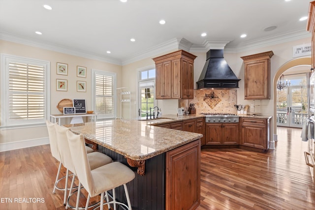 kitchen with sink, kitchen peninsula, stainless steel gas stovetop, custom range hood, and hardwood / wood-style flooring