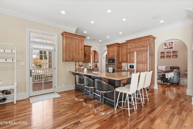 kitchen with light stone countertops, stainless steel appliances, crown molding, hardwood / wood-style floors, and a kitchen bar