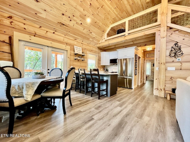 dining space with wood walls, high vaulted ceiling, wood ceiling, light wood-type flooring, and french doors