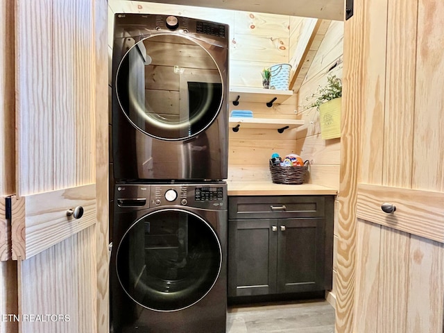 laundry room with cabinets, light hardwood / wood-style flooring, wooden walls, and stacked washer / dryer