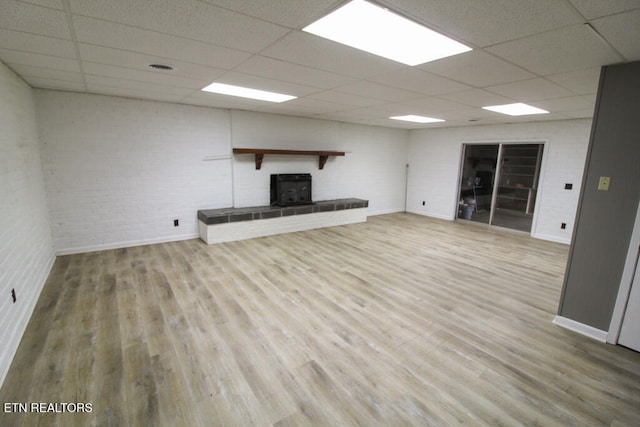 unfurnished living room featuring a drop ceiling, wood-type flooring, and a wood stove