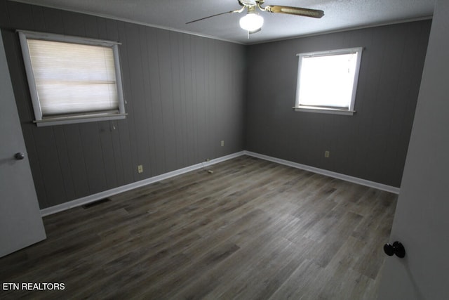 empty room featuring ornamental molding, wooden walls, ceiling fan, and dark wood-type flooring