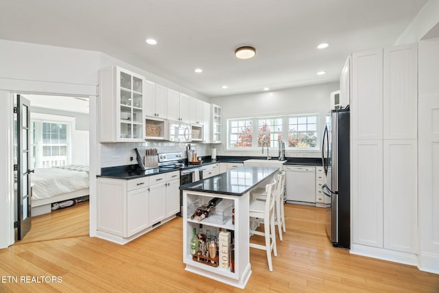 kitchen with backsplash, stainless steel appliances, white cabinetry, light hardwood / wood-style flooring, and a kitchen island