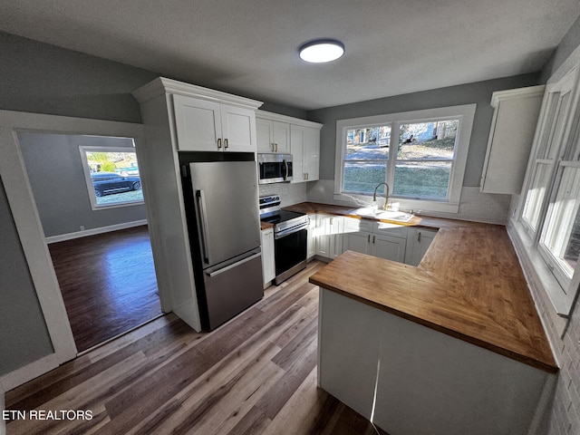 kitchen featuring sink, kitchen peninsula, light hardwood / wood-style floors, white cabinets, and appliances with stainless steel finishes