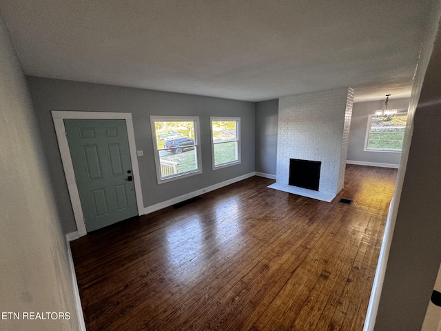 unfurnished living room with a fireplace, plenty of natural light, dark wood-type flooring, and a notable chandelier