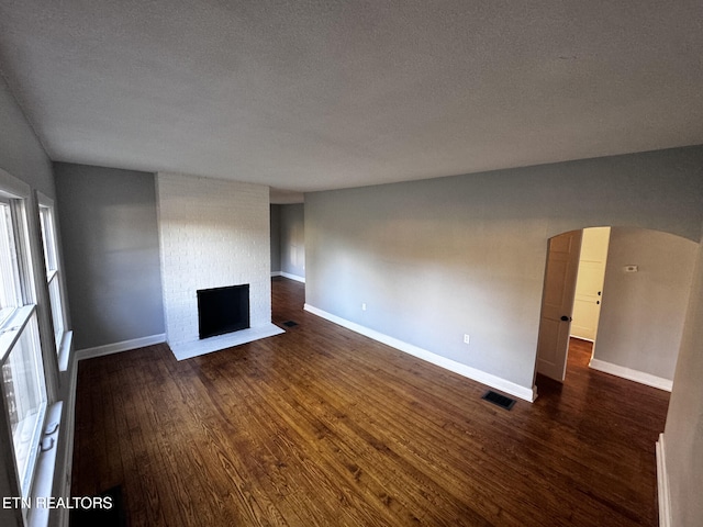 unfurnished living room featuring a textured ceiling, dark hardwood / wood-style floors, and a brick fireplace