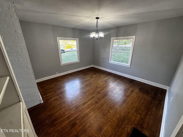 unfurnished dining area featuring an inviting chandelier, dark hardwood / wood-style flooring, and a textured ceiling