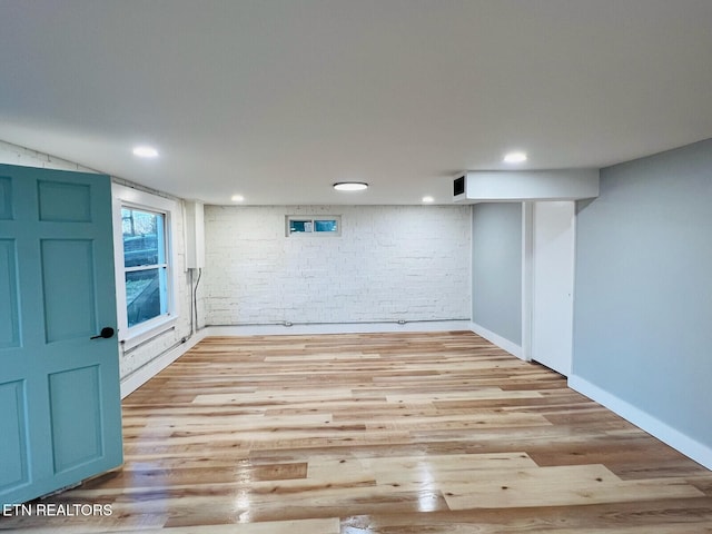 basement with brick wall and light wood-type flooring