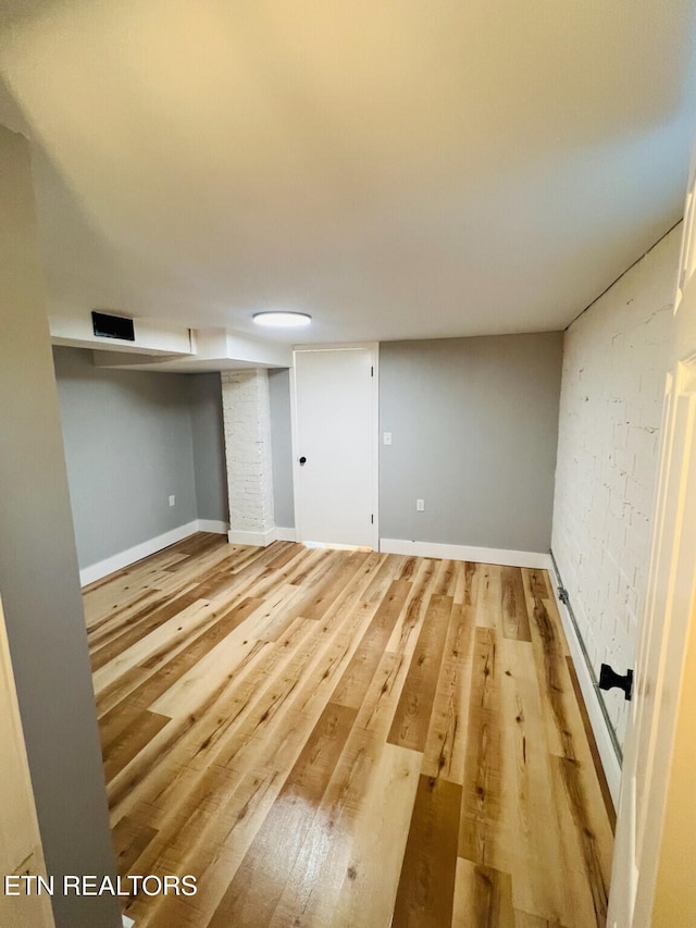 basement with brick wall and hardwood / wood-style flooring