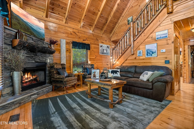 living room featuring wood-type flooring, a stone fireplace, beam ceiling, wood walls, and wooden ceiling