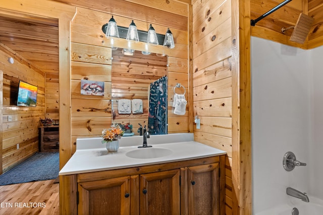 bathroom featuring hardwood / wood-style floors, vanity, wooden walls, and shower / bathtub combination