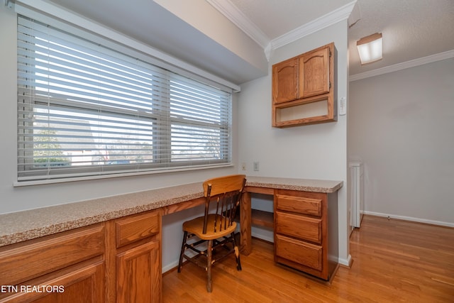 office area with light wood-type flooring, built in desk, and crown molding