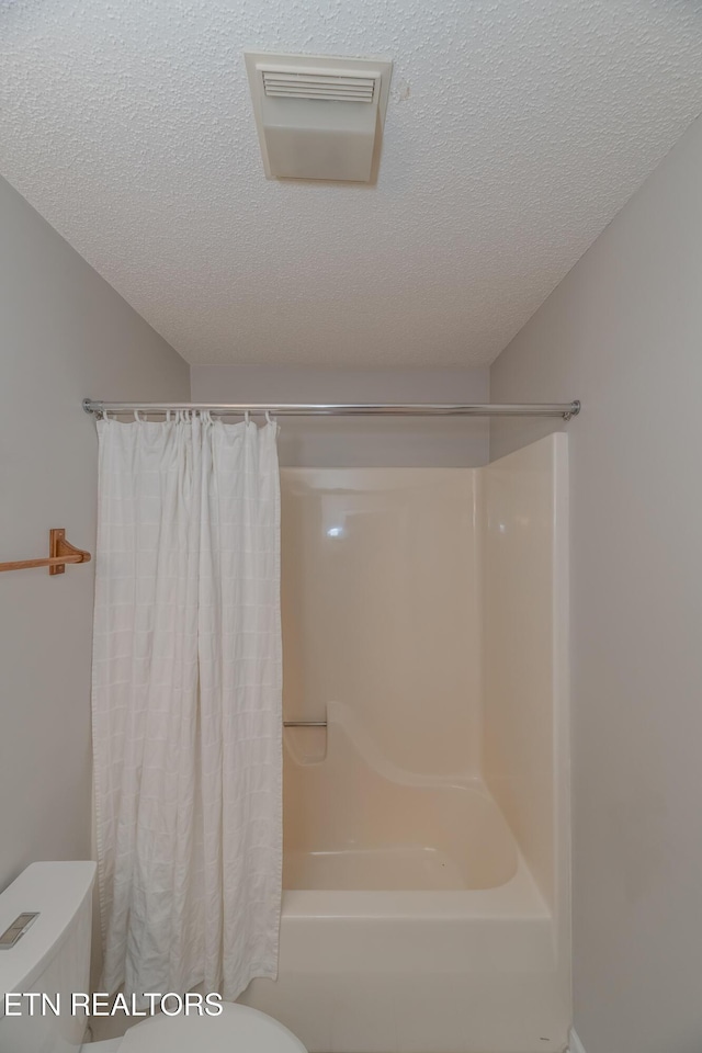 bathroom with shower / bath combination with curtain, a textured ceiling, and toilet