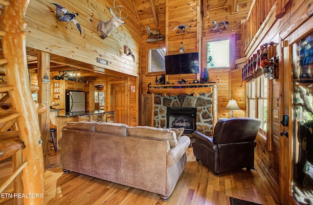 living room featuring wooden ceiling, wooden walls, light hardwood / wood-style flooring, a fireplace, and beamed ceiling