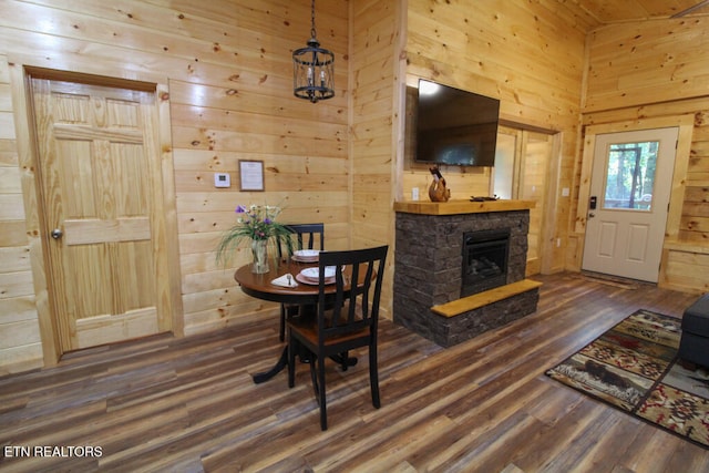 dining area with dark hardwood / wood-style flooring, a stone fireplace, and wood walls