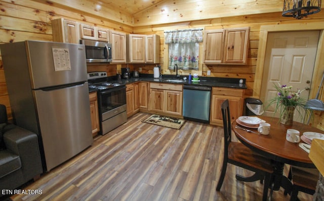 kitchen with hardwood / wood-style floors, sink, wooden walls, vaulted ceiling, and stainless steel appliances