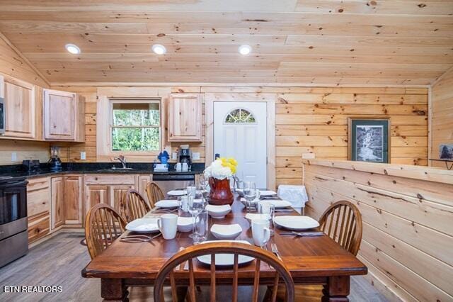 dining space featuring light wood-type flooring, wood ceiling, wooden walls, sink, and lofted ceiling