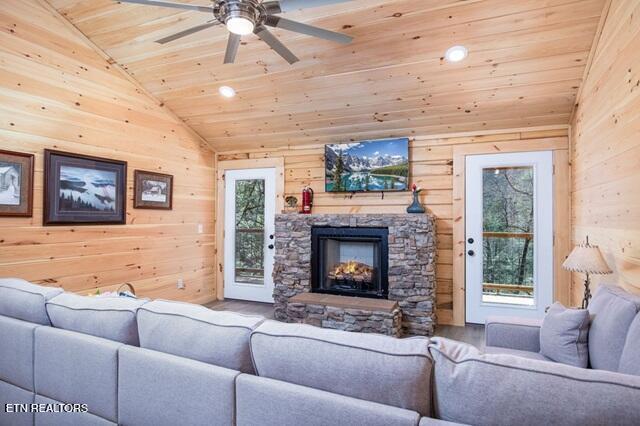 living room with lofted ceiling, a stone fireplace, wooden walls, ceiling fan, and wood ceiling