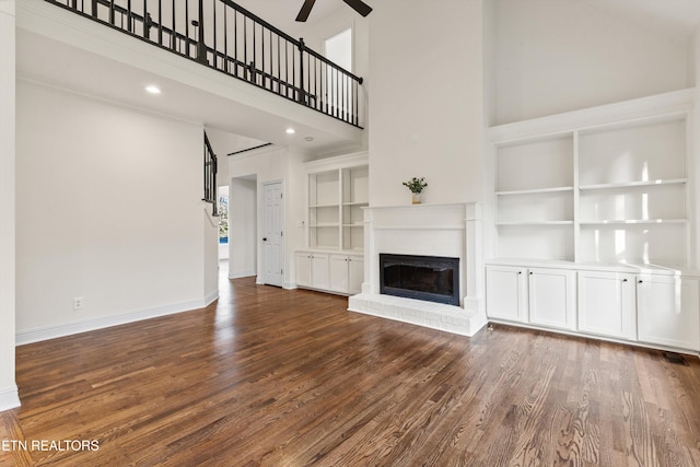 unfurnished living room with a fireplace, a towering ceiling, ceiling fan, and dark wood-type flooring