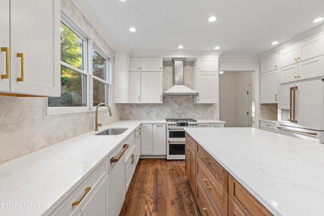 kitchen featuring high end appliances, white cabinets, wall chimney range hood, sink, and light stone counters