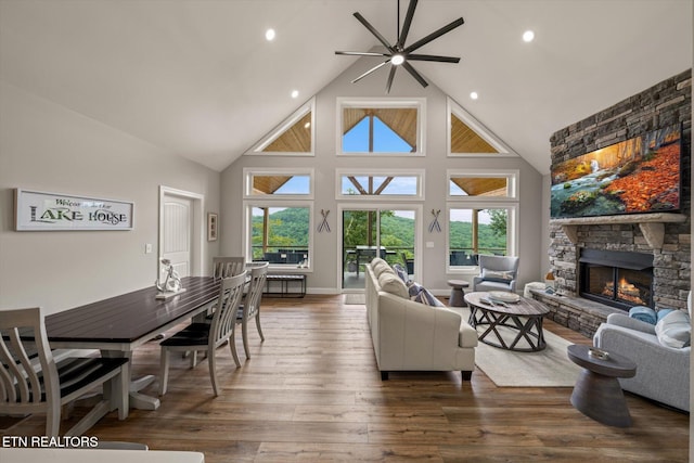 living room featuring a stone fireplace, high vaulted ceiling, a wealth of natural light, and dark hardwood / wood-style floors