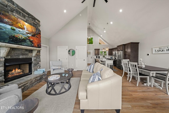 living room featuring high vaulted ceiling, light wood-type flooring, ceiling fan, and a fireplace