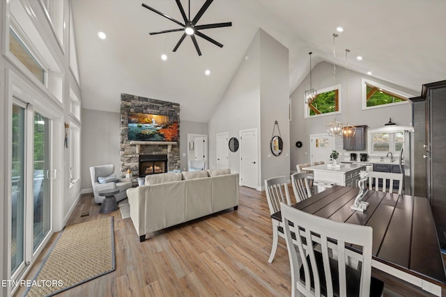 dining space with a wealth of natural light, a stone fireplace, light hardwood / wood-style flooring, and high vaulted ceiling