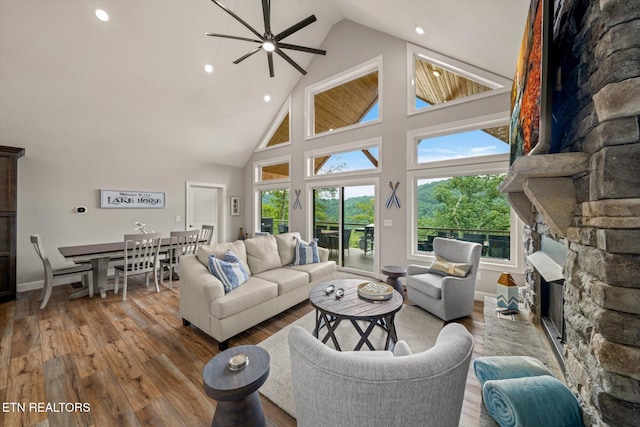 living room with a fireplace, light hardwood / wood-style floors, ceiling fan, and high vaulted ceiling