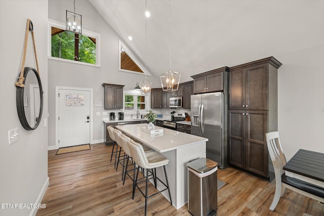 kitchen with stainless steel appliances, light hardwood / wood-style floors, a center island, high vaulted ceiling, and decorative light fixtures