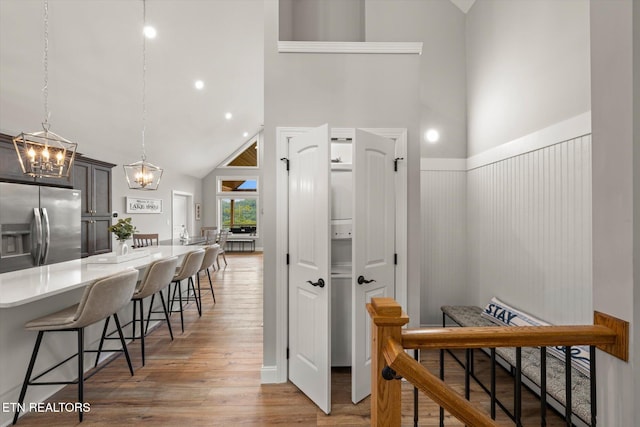 kitchen with hardwood / wood-style flooring, a breakfast bar area, high vaulted ceiling, hanging light fixtures, and stainless steel fridge