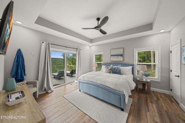 bedroom featuring access to outside, a tray ceiling, wood-type flooring, and ceiling fan