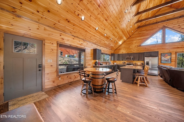 dining room with wooden walls, a healthy amount of sunlight, high vaulted ceiling, and light hardwood / wood-style flooring