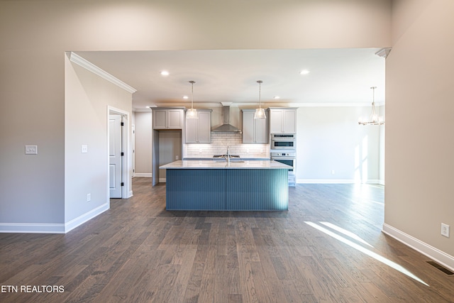 kitchen featuring dark hardwood / wood-style floors, hanging light fixtures, wall chimney exhaust hood, and an island with sink