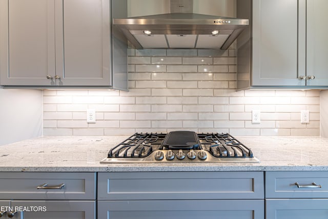 kitchen featuring stainless steel gas stovetop, backsplash, gray cabinets, light stone countertops, and extractor fan