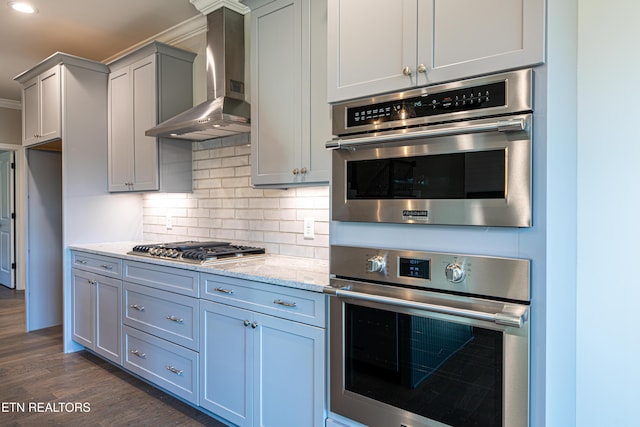 kitchen featuring appliances with stainless steel finishes, backsplash, light stone counters, wall chimney exhaust hood, and dark wood-type flooring