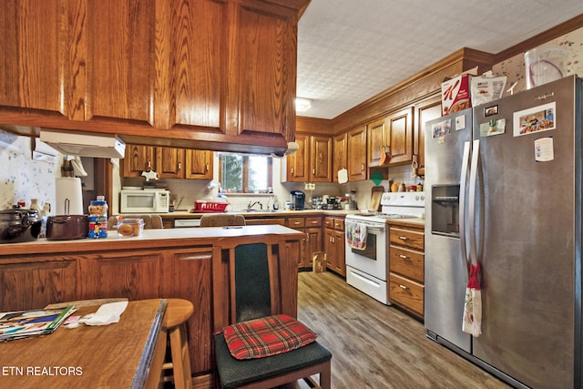 kitchen featuring kitchen peninsula, crown molding, hardwood / wood-style floors, and white appliances