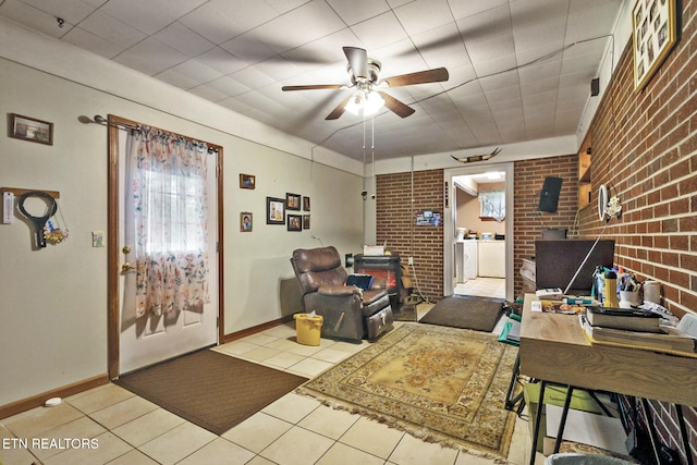 living room featuring ceiling fan, light tile patterned flooring, washer and dryer, and brick wall