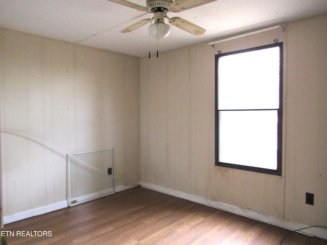 empty room featuring ceiling fan, wooden walls, and dark hardwood / wood-style floors