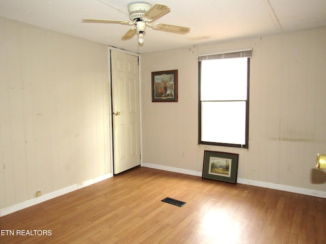 empty room with light wood-type flooring, ceiling fan, and wood walls