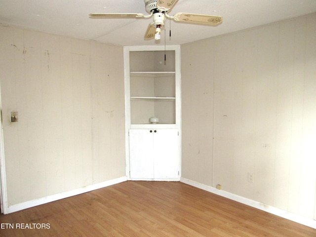 spare room with hardwood / wood-style flooring, ceiling fan, and wooden walls