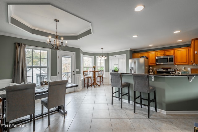 kitchen with appliances with stainless steel finishes, crown molding, a tray ceiling, and a breakfast bar