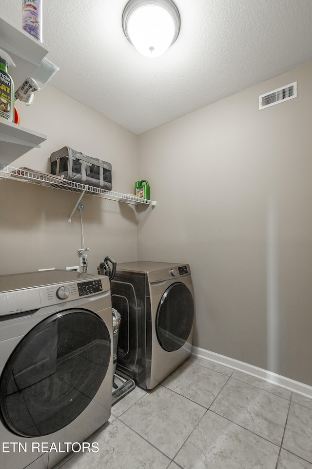 laundry room with a textured ceiling, independent washer and dryer, and light tile patterned flooring