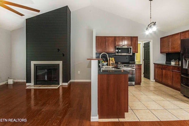 kitchen with a large fireplace, light hardwood / wood-style floors, pendant lighting, vaulted ceiling, and appliances with stainless steel finishes