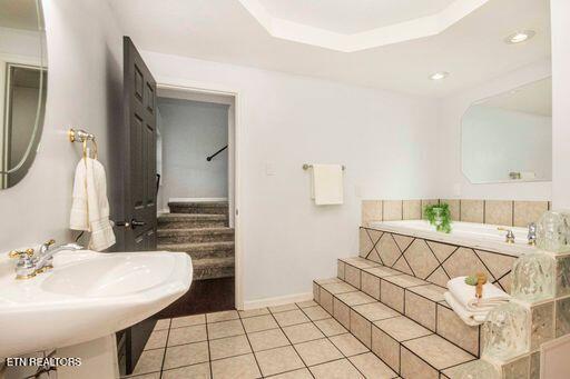 bathroom with tile patterned floors, tiled tub, and a tray ceiling