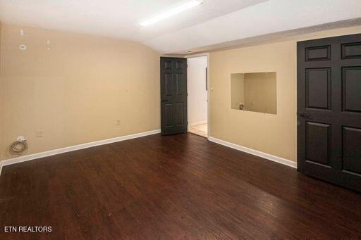 spare room with dark wood-type flooring and lofted ceiling